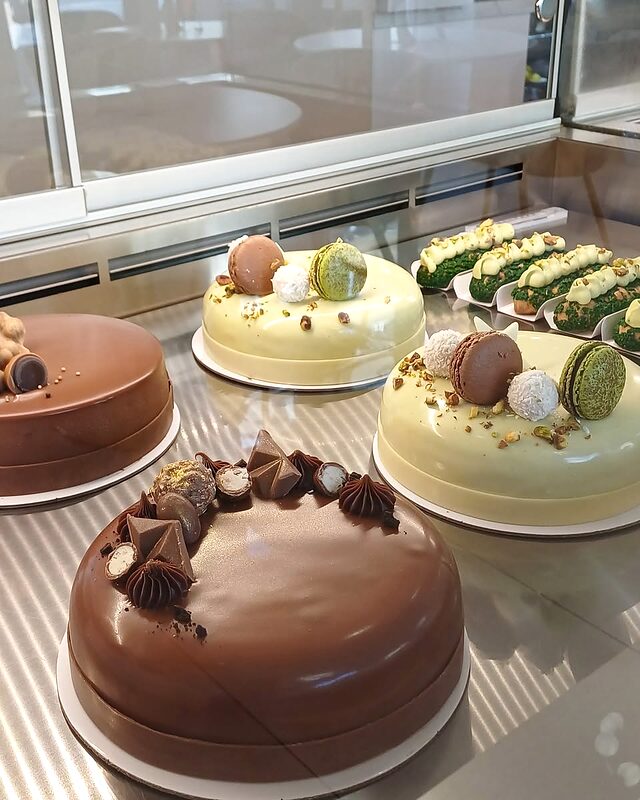 Vitrina cofetăriei, cu un tort de ciocolată și prăjituri cu macarons