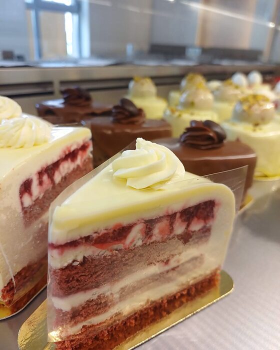 Felie de tort cu fructe roșii, cremă albă și blat însiropat